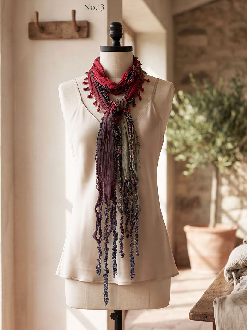 A long, multi-colored scarf with tassel fringe and patterned strands by Monkey Mango, styled on a cream-colored mannequin torso. The scarf features shades of red, purple, green, and blue.