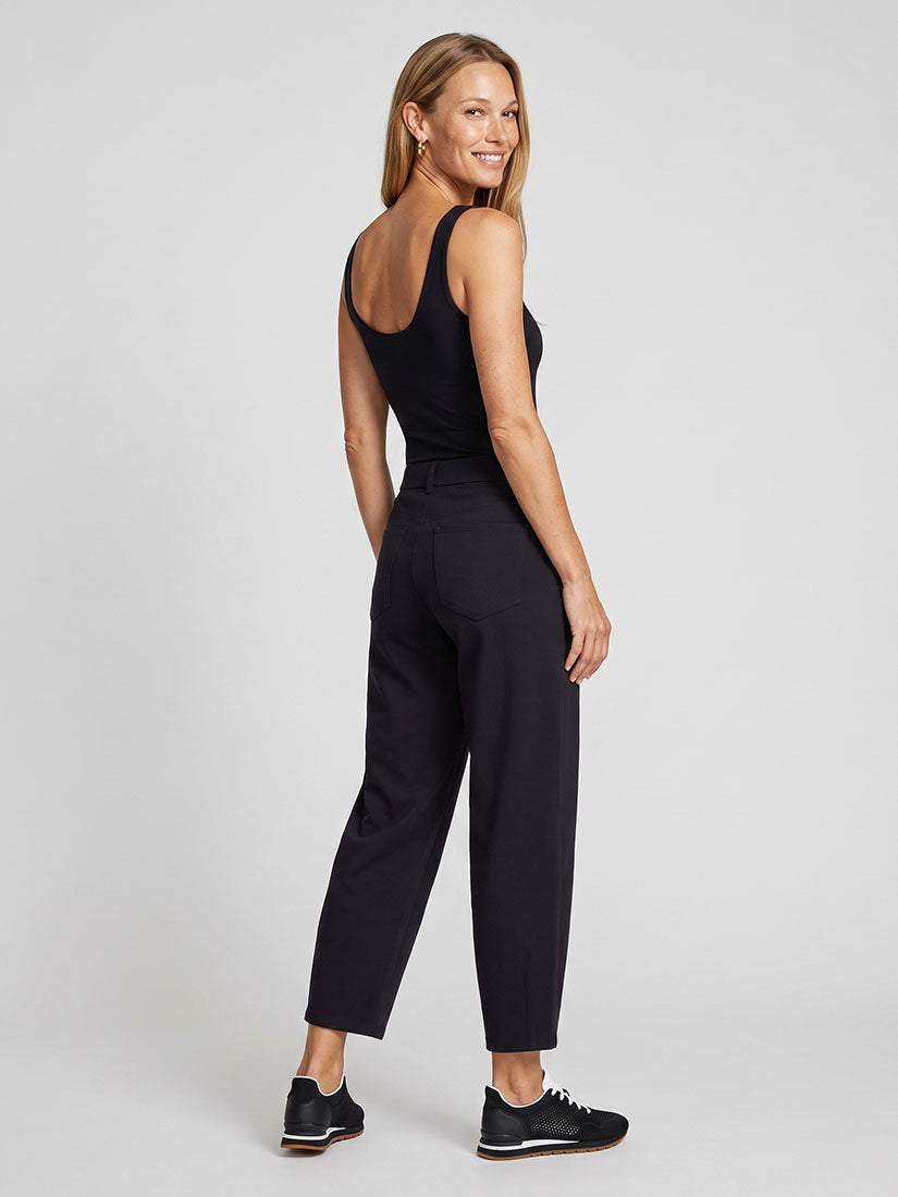 A woman modeling a black sleeveless top and black cropped trousers, shown from a three-quarters back view against a light gray studio background.