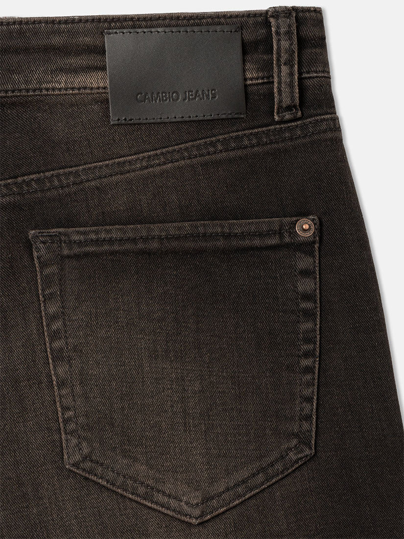 Close-up of the back waistband and pocket area of dark charcoal gray denim jeans, showing a black leather patch with the embossed brand name CAMBIO JEANS.