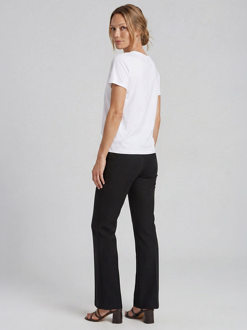 A woman modeling a white short-sleeve crewneck t-shirt and black wide-leg pants, shown from a rear three-quarter angle against a light gray studio background.