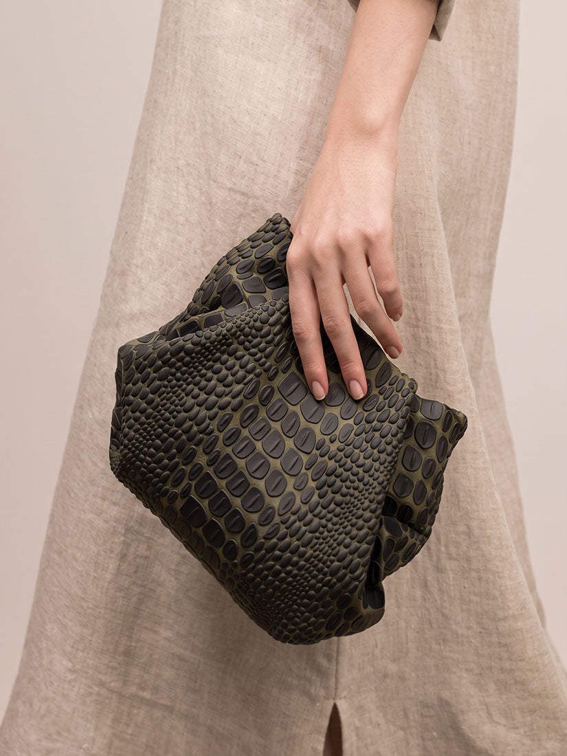 Person holding a croc textured green and black clutch bag against a neutral background