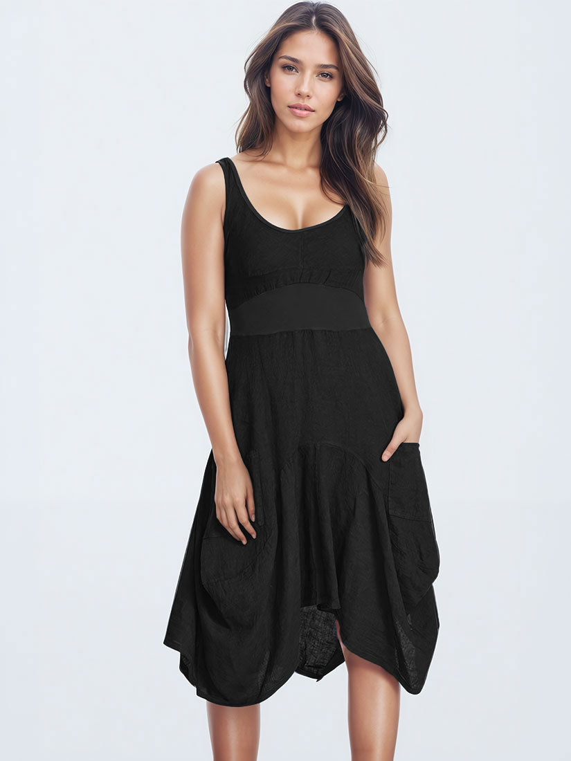A woman modeling a sleeveless black midi dress with a scoop neckline, a wide waistband, and a tiered skirt with side pockets, set against a plain light gray studio background.