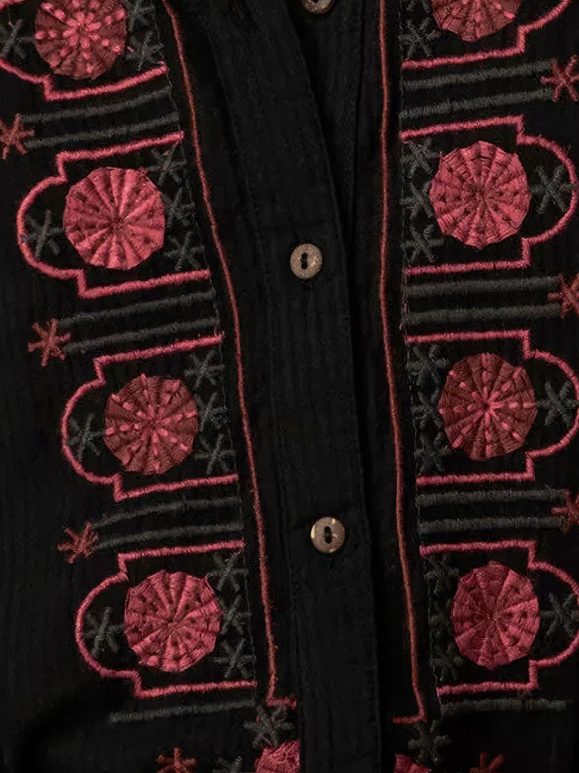 Close-up of a black button-front garment with ornate pink and red embroidered geometric and floral patterns on both sides of the front opening.