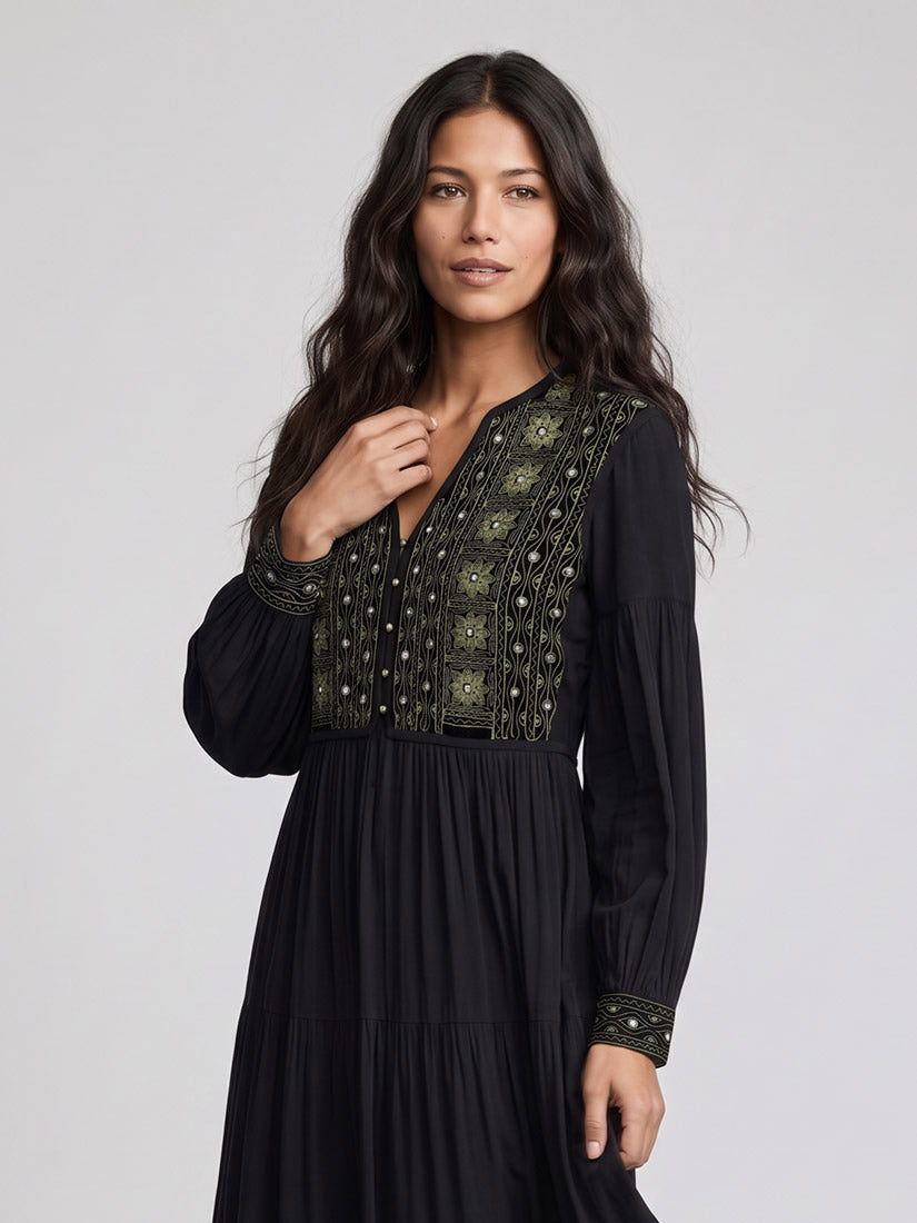 dark haired woman in black embroisered maxi dress showing embroider detail in studio setting