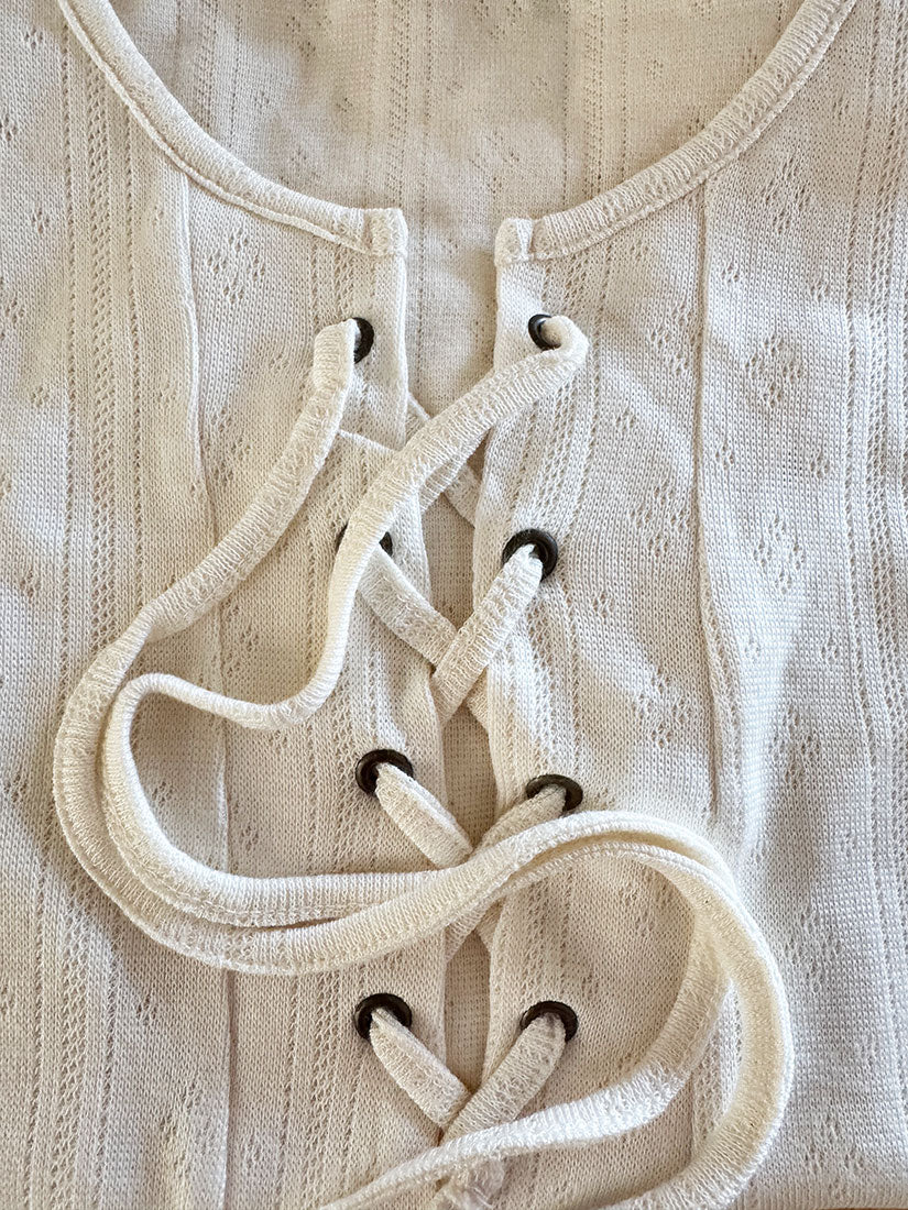 Close-up of a cream-colored textured knit top with a lace-up front closure and black eyelets.