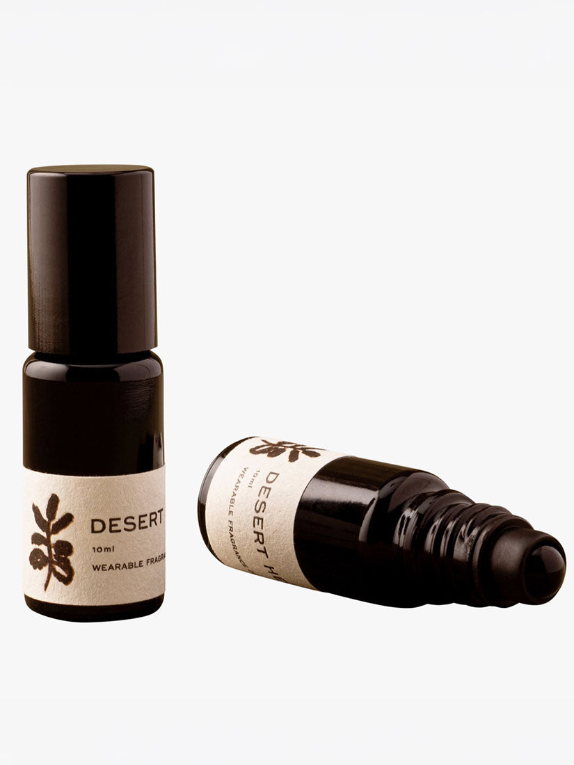 Two small dark amber glass bottles with white labels reading DESERT WARMING SPICE, one standing upright and one lying on its side, on a light gray background.