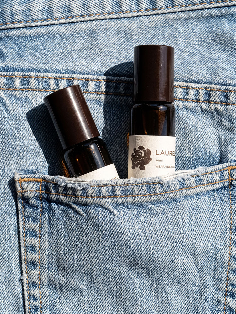 Two small dark amber perfume or fragrance bottles with white labels tucked into the back pocket of light blue denim jeans. One label clearly reads LAUREN.