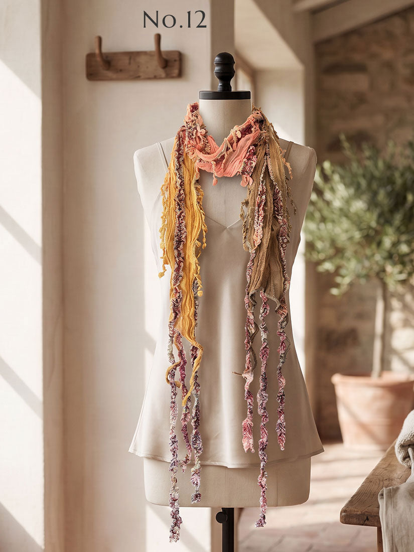 A multicolor fringed scarf by Monkey Mango with yellow, pink, and floral patterns displayed on a beige dress form mannequin in a warm, sunlit room.