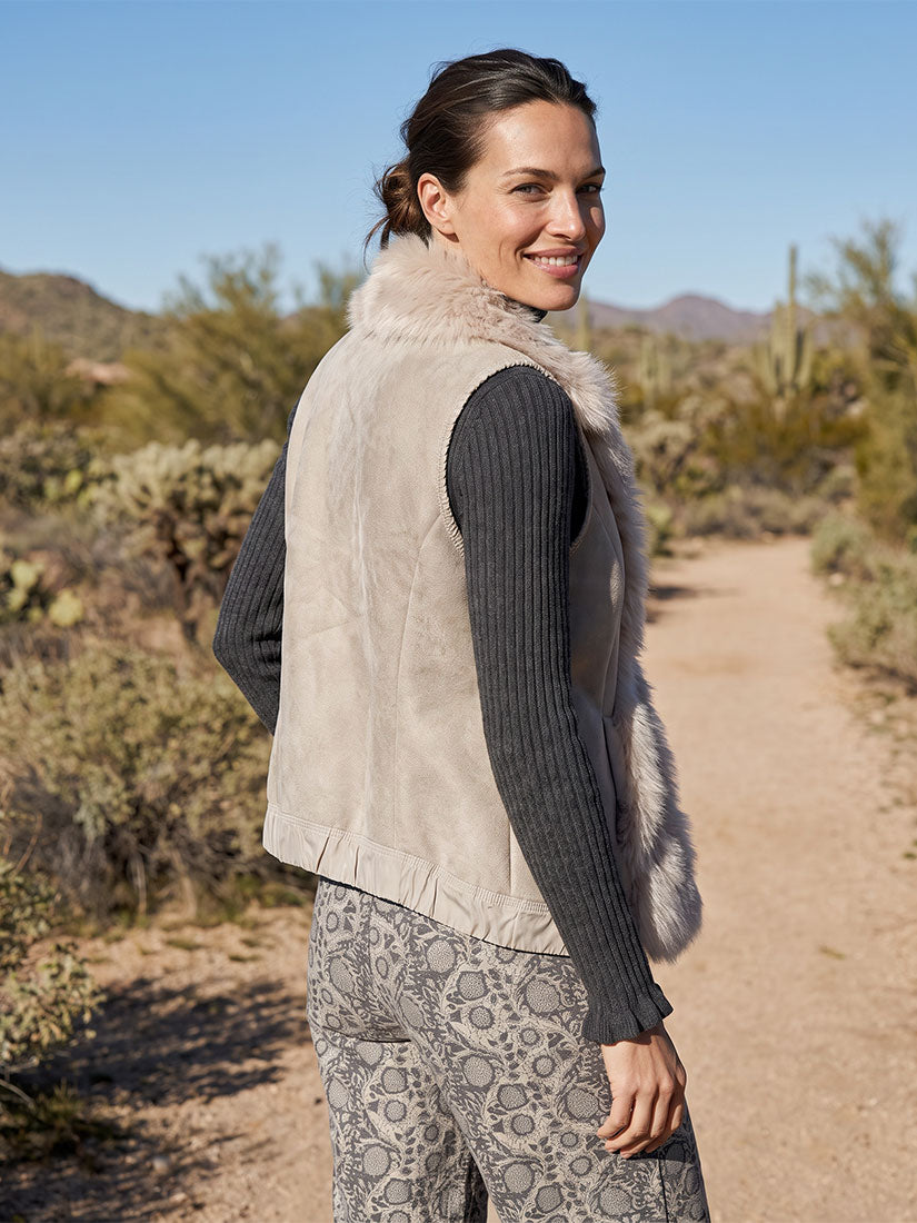 woman with dark hair wearing fleece and faux fur vest. back vuew