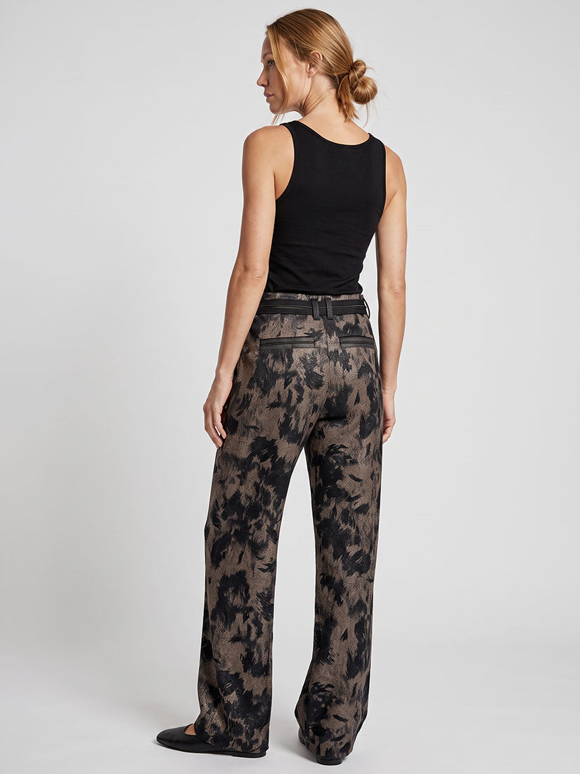 A woman shown from the back wearing a black sleeveless top and high-waisted wide-leg trousers with a dark brown and black abstract floral pattern, photographed against a light gray studio background.