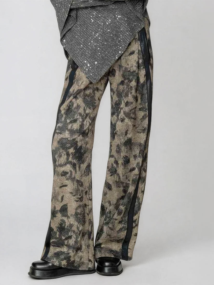 A person wearing wide-leg pants with an abstract black and beige pattern, black side panels, and black shoes, photographed against a light gray studio background.