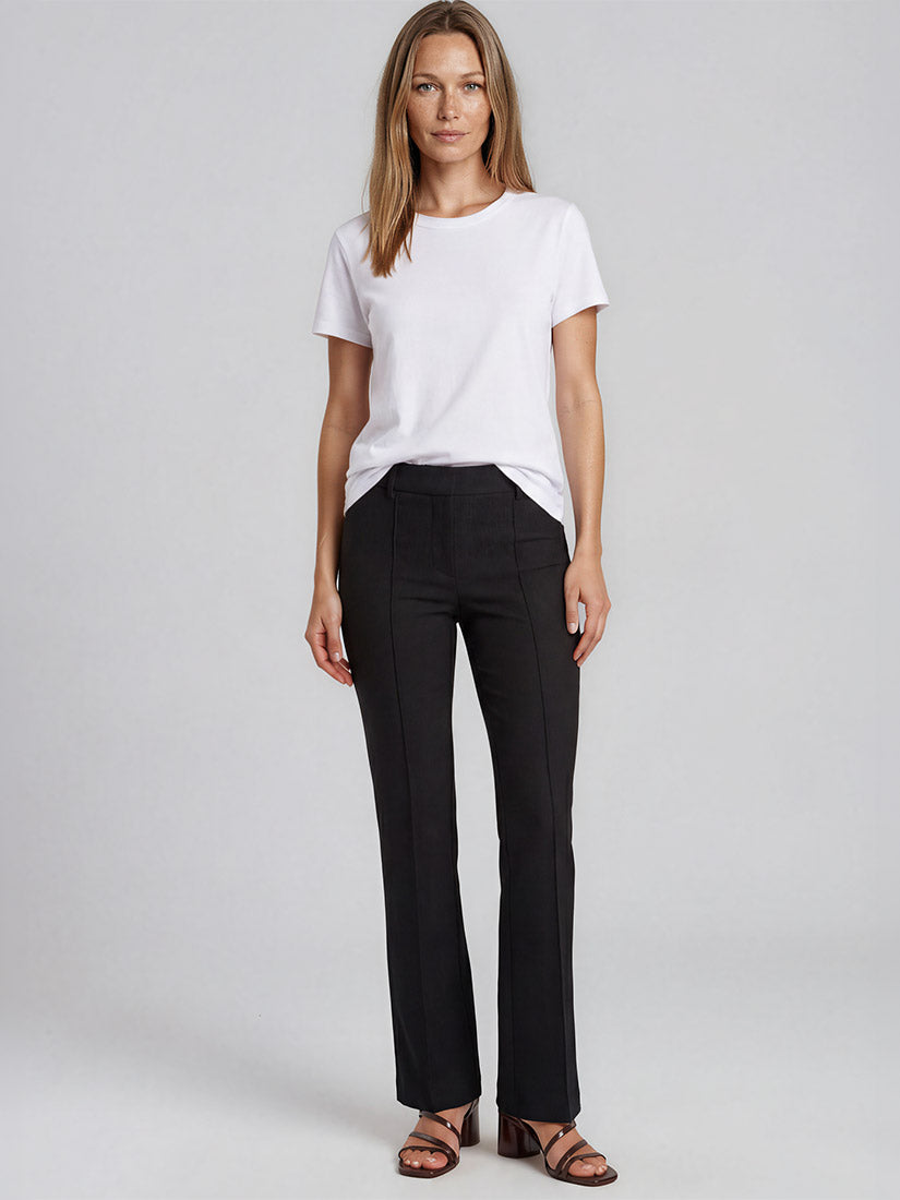 A woman modeling a white short-sleeve crewneck t-shirt and black cambio straight-leg trousers, paired with brown strappy sandals, against a light gray studio background.