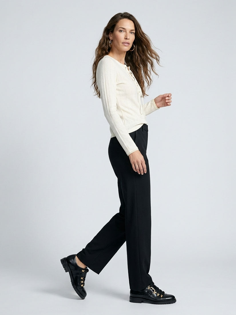 A woman modeling a cream ribbed long-sleeve top and black wide-leg trousers, paired with black lace-up shoes, against a light gray studio background.