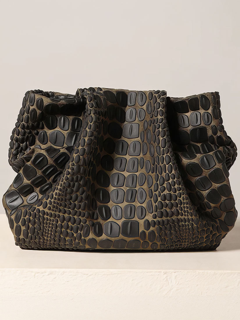 A textured shoulder bag with a dark olive green and black crocodile-embossed pattern, displayed on a light beige surface against a neutral background.