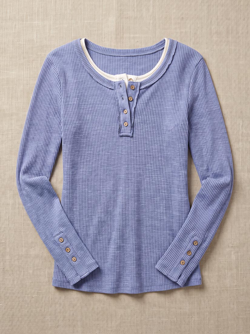 A light blue and white micro-check long-sleeve henley shirt with brown buttons, laid flat on a beige textured fabric background.