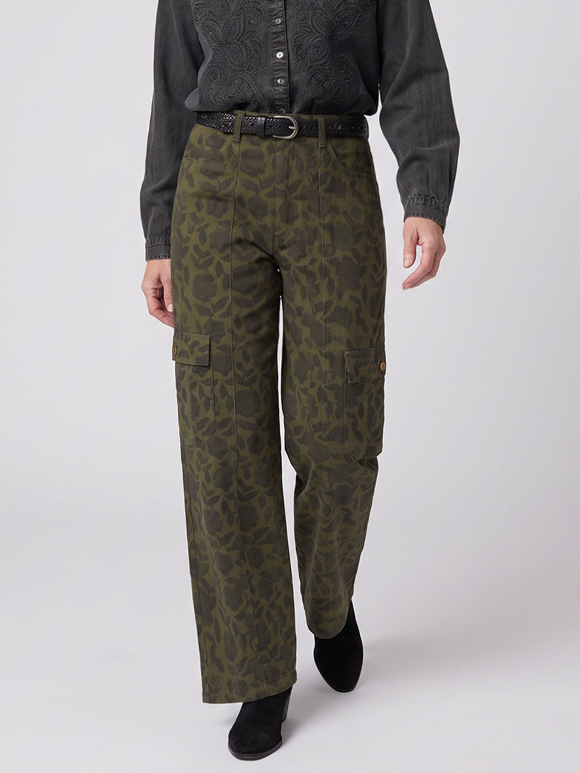 A person wearing Alan olive green cargo pants with an allover tonal floral pattern by maison hotel, styled with a black belt, a dark gray long-sleeve shirt, and black shoes against a light gray studio background.