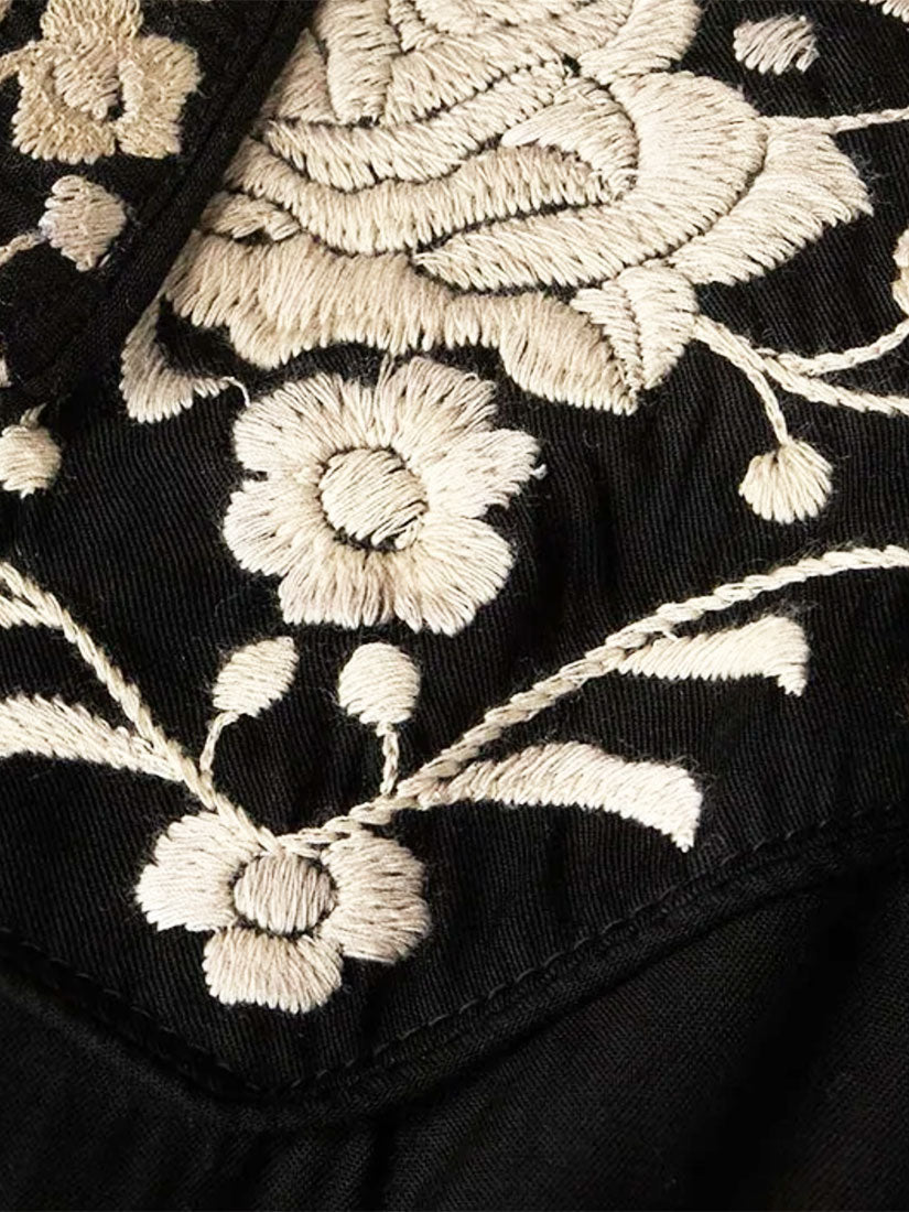 Close-up of black fabric with cream floral embroidery, showing detailed threadwork and stitched edges.