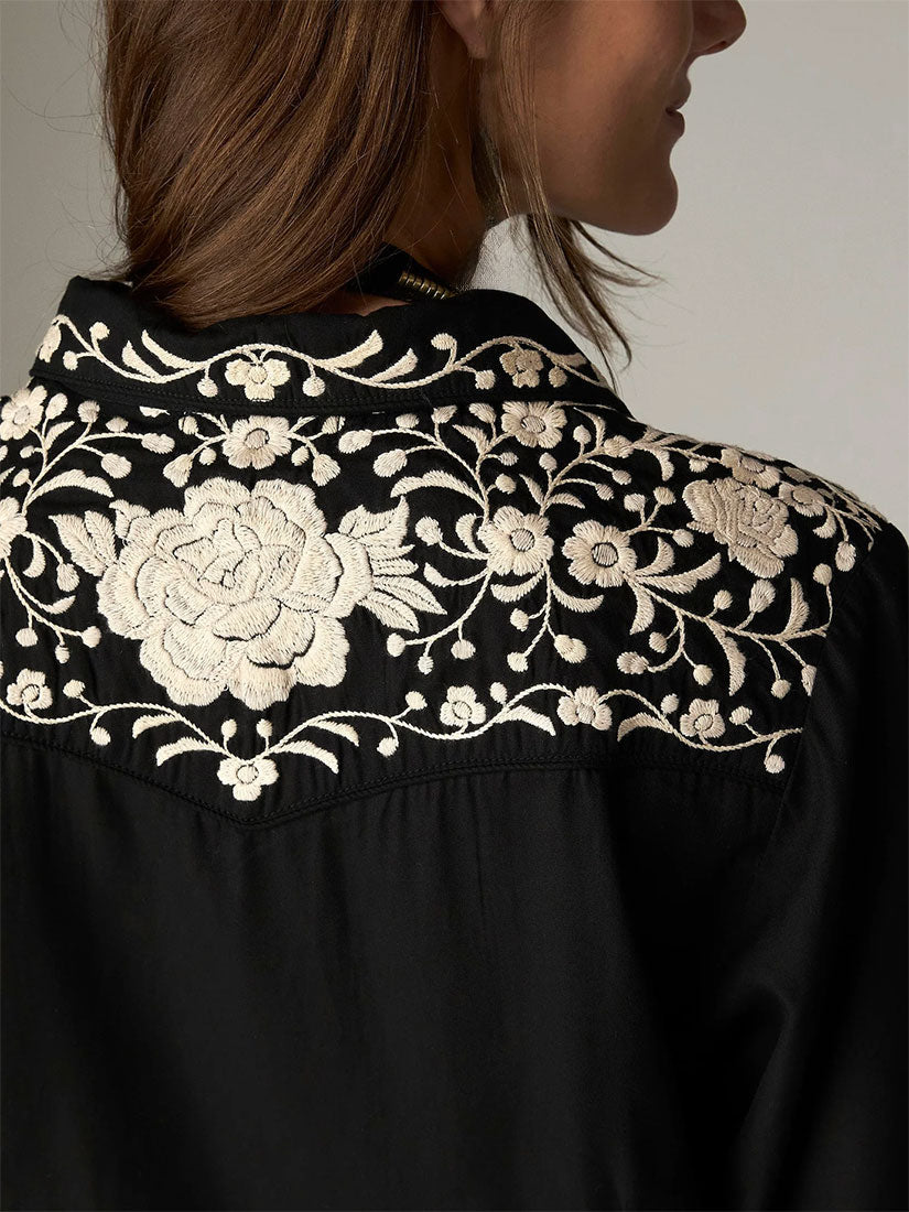Close-up of a woman wearing a black blouse with intricate cream floral embroidery across the yoke and shoulders by maison hotel