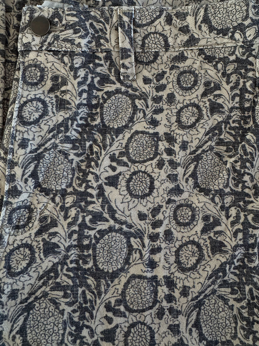 Close-up of a patterned fabric garment, likely shorts or pants, featuring a dark navy blue floral and botanical print on a light beige background.