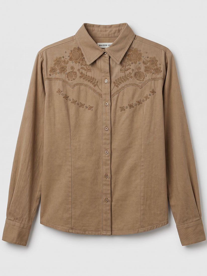 A tan long-sleeve western-style button-up shirt with embroidered floral patterns across the chest, displayed on a neutral light gray background.