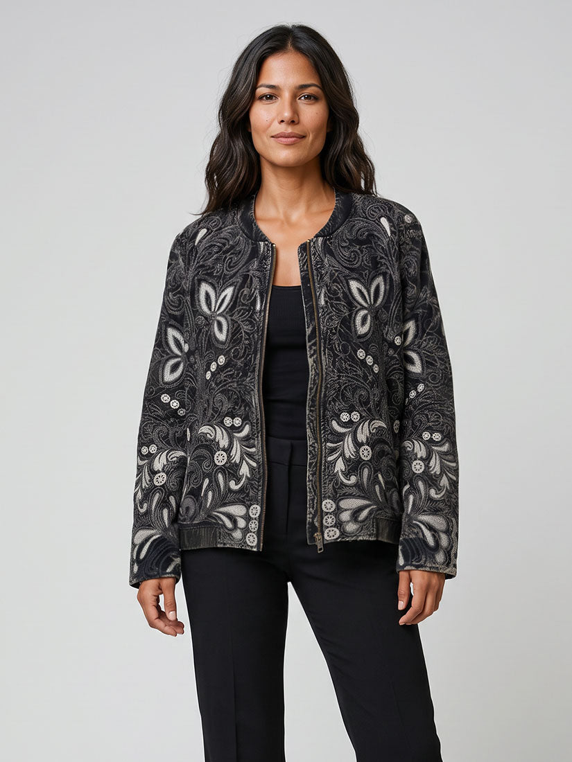 A woman modeling a black and white patterned bomber jacket over a black top and black pants, photographed against a light gray studio background.