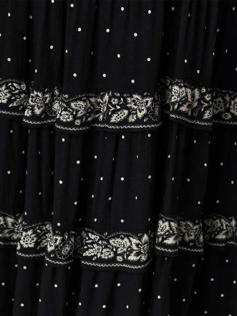 Close-up of a black tiered skirt with small white polka dots and ornate white floral lace trim along horizontal ruffles.