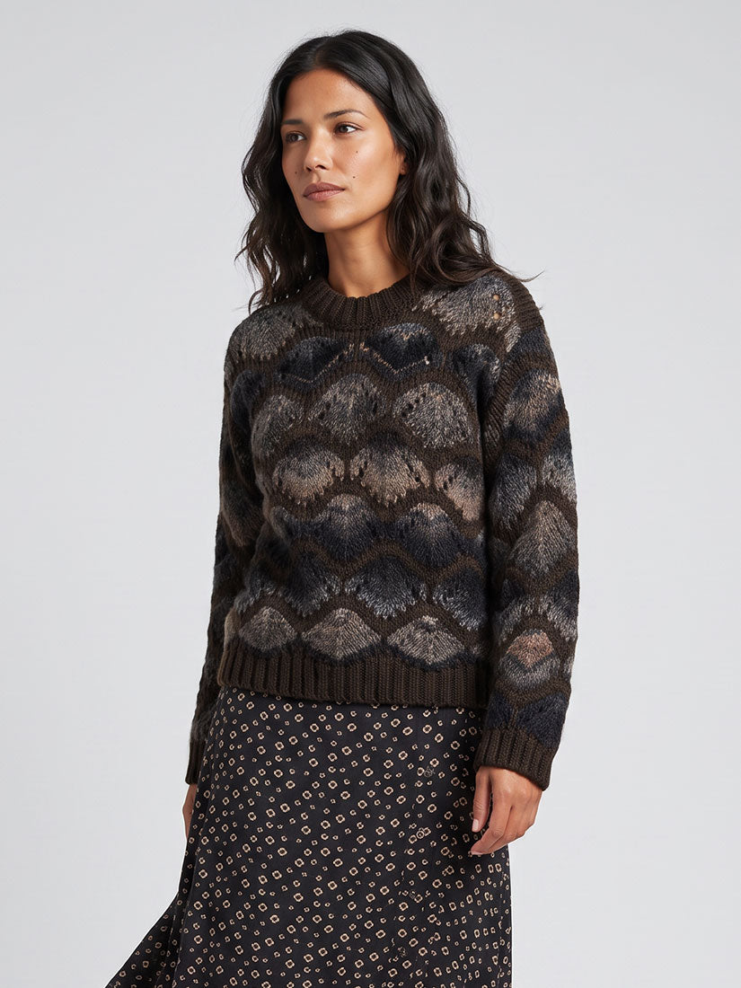 A woman wearing a dark brown and charcoal patterned knit sweater with a matching dark patterned skirt, photographed against a light gray studio background.