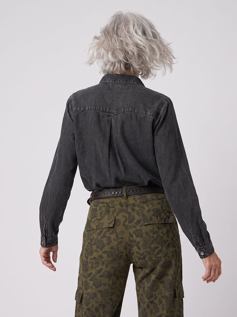 A model from behind wearing a washed black denim shirt and olive green patterned cargo pants, shown against a light gray studio background.