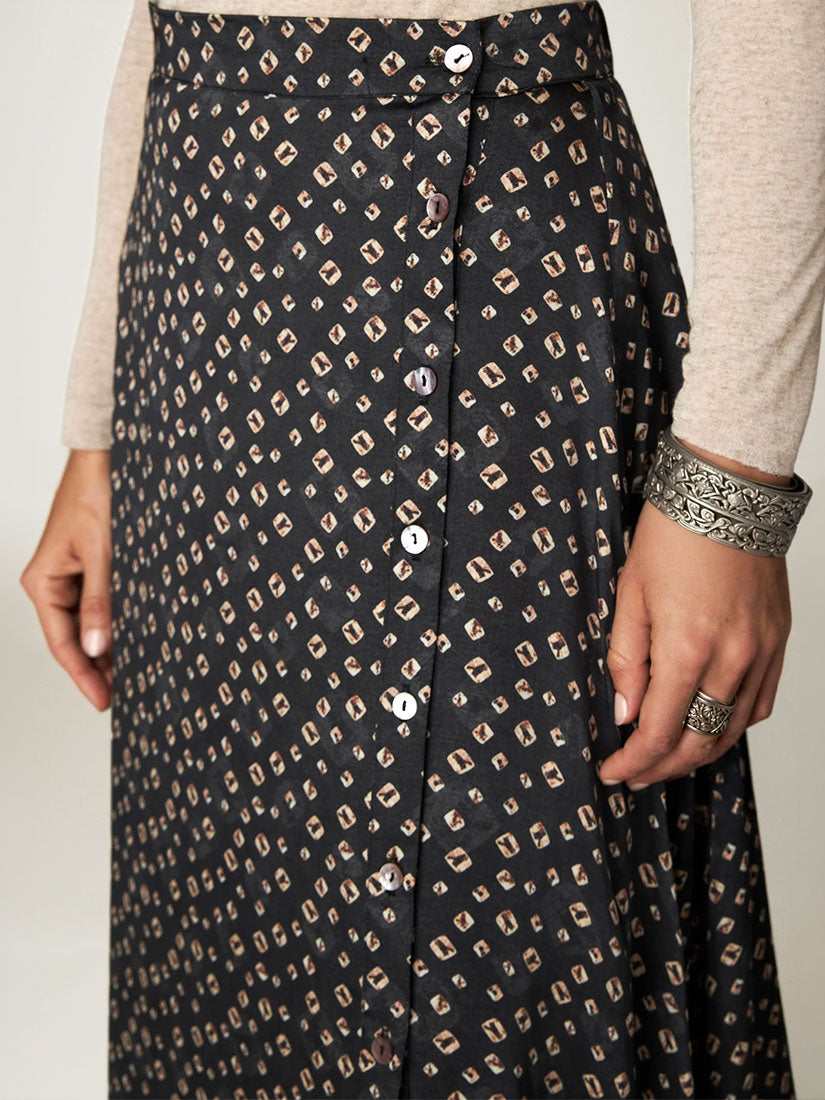 A close-up of a black midi skirt with a beige and brown geometric print, featuring a button-down front and worn with a beige long-sleeve top.