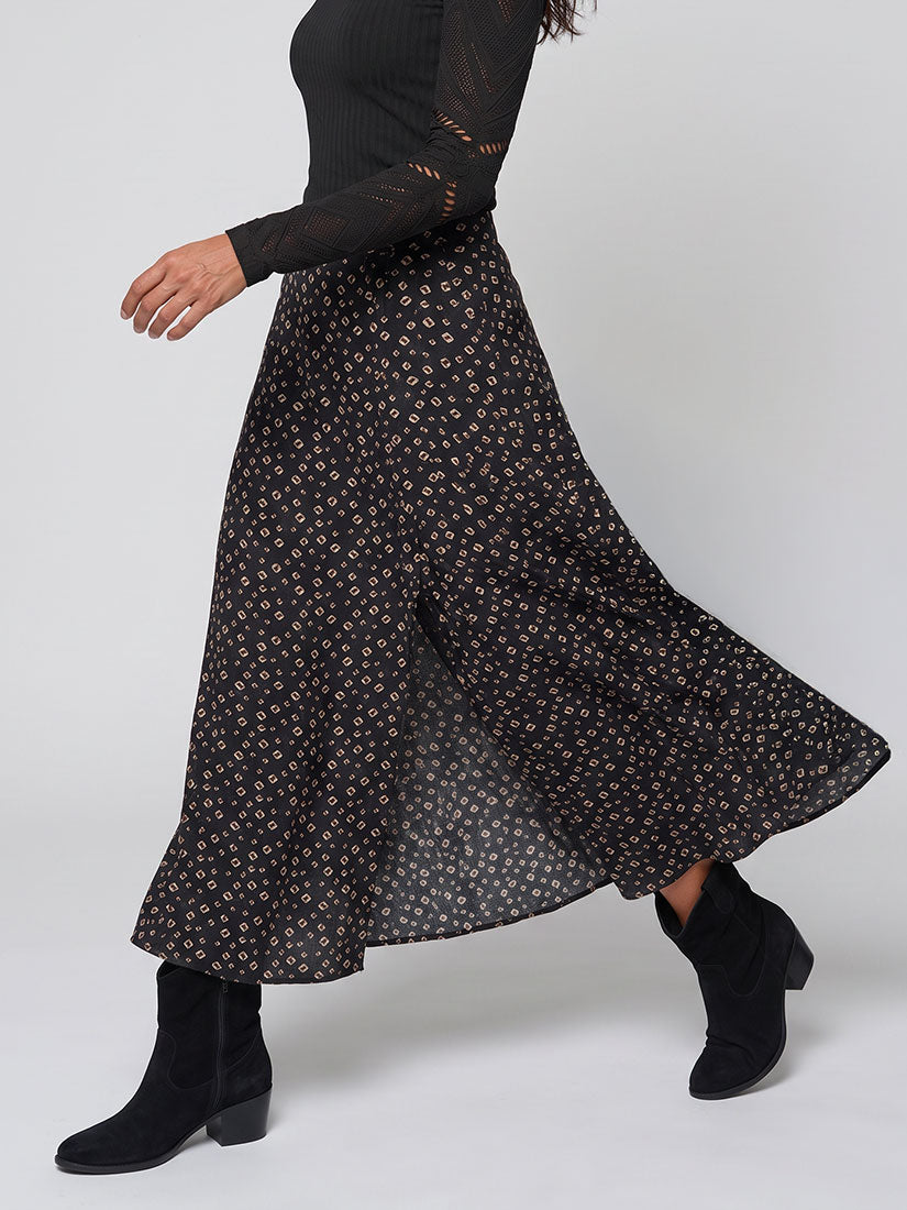 A black midi skirt with a small beige floral pattern, worn by a model in a black long-sleeve top and black ankle boots against a light gray studio background.