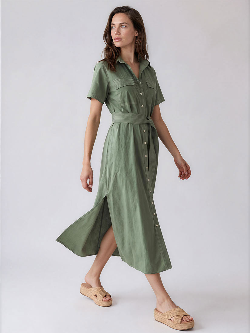 A woman modeling a short-sleeve olive green midi shirt dress with a matching waist belt and front button placket, paired with tan slide sandals, against a light gray studio background.